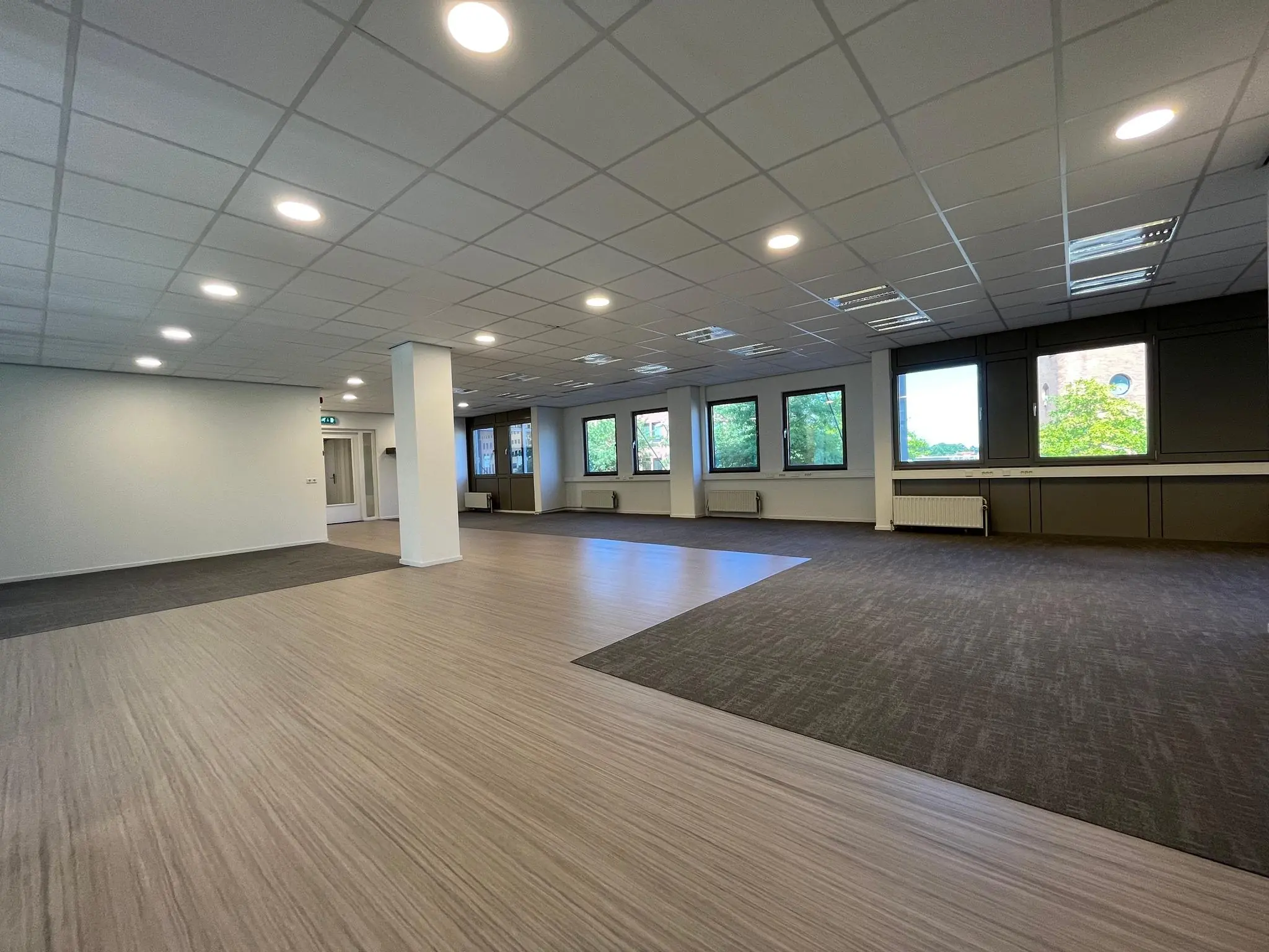 Ruim, modern kantoorpand aan de Barchman Wuytierslaan met grote ramen, systeemplafond en gemengd vloeroppervlak van tapijt en laminaat.